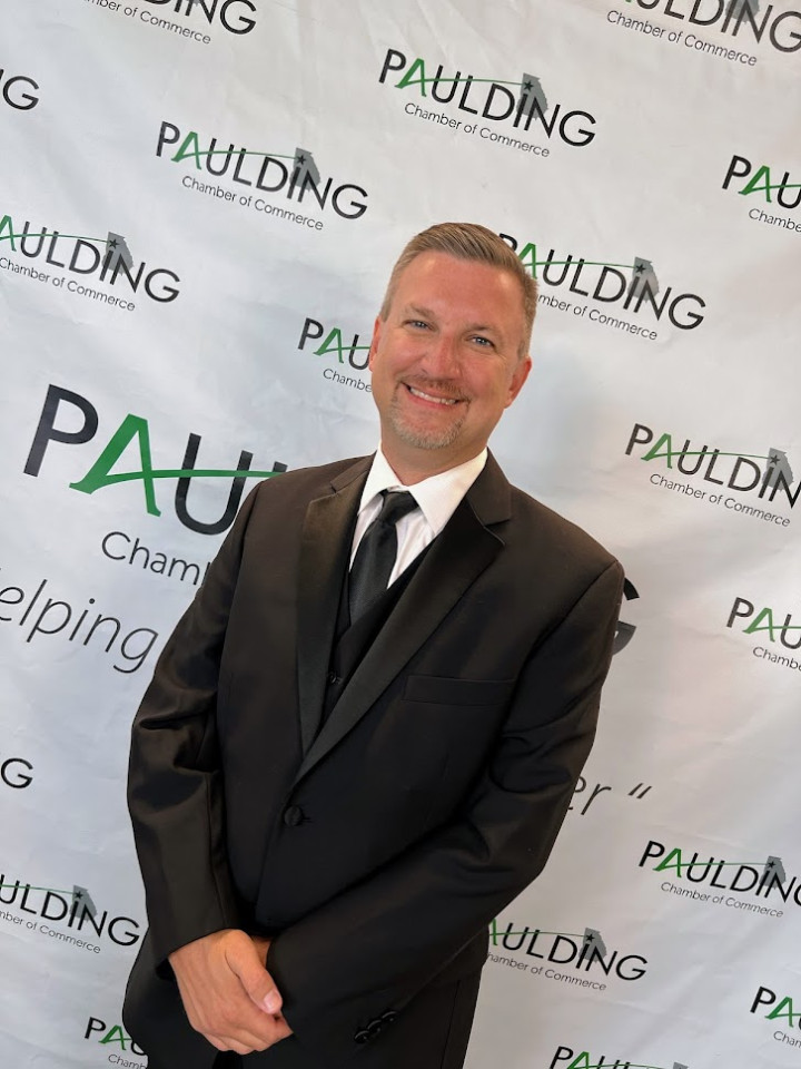 Greg Perry stands in front of a step-and-repeat in a suit